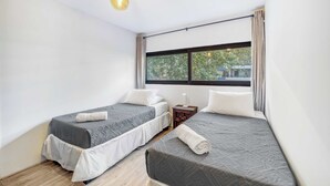 Une chambre avec deux lits, une fenêtre avec des rideaux, une petite table de chevet et un luminaire suspendu.