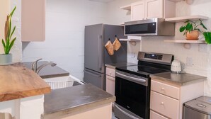 Eine moderne Küche mit einem Edelstahl-Kühlschrank, Backofen und einer Mikrowelle. Es gibt eine Holz Arbeitsplatte und ein Spülbecken mit Wasserhahn.