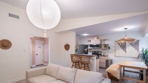 Ein modernes Wohnzimmer mit Sofa, Esstisch und einer Küche im Hintergrund.
