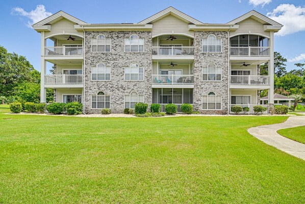 Un edificio de varios pisos con balcones, fachada de piedra y un césped bien cuidado.