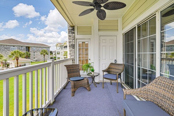 A balcony with wicker furniture, a ceiling fan, and a view of neighboring buildings.