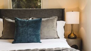 A neatly made bed with a grey headboard, a blue pillow, and a grey pillow. There is a bedside lamp on a small table beside the bed. - Spacious Craftsman Home | Family friendly | Arcade  | 5 Bedrooms (Portland)