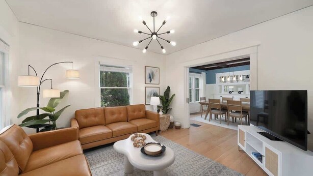 A modern living room with a leather sofa, a coffee table, a TV, and a dining area with chairs and a table. - Spacious Craftsman Home | Family friendly | Arcade  | 5 Bedrooms (Portland)