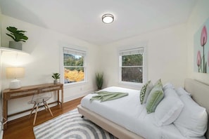 Ein Schlafzimmer mit Bett, Nachttisch, Lampe und Fenstern.