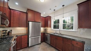 A modern kitchen with dark wooden cabinets, stainless steel appliances, and a large window providing natural light. - Spacious Craftsman Home | Family friendly | Arcade  | 5 Bedrooms (Portland)