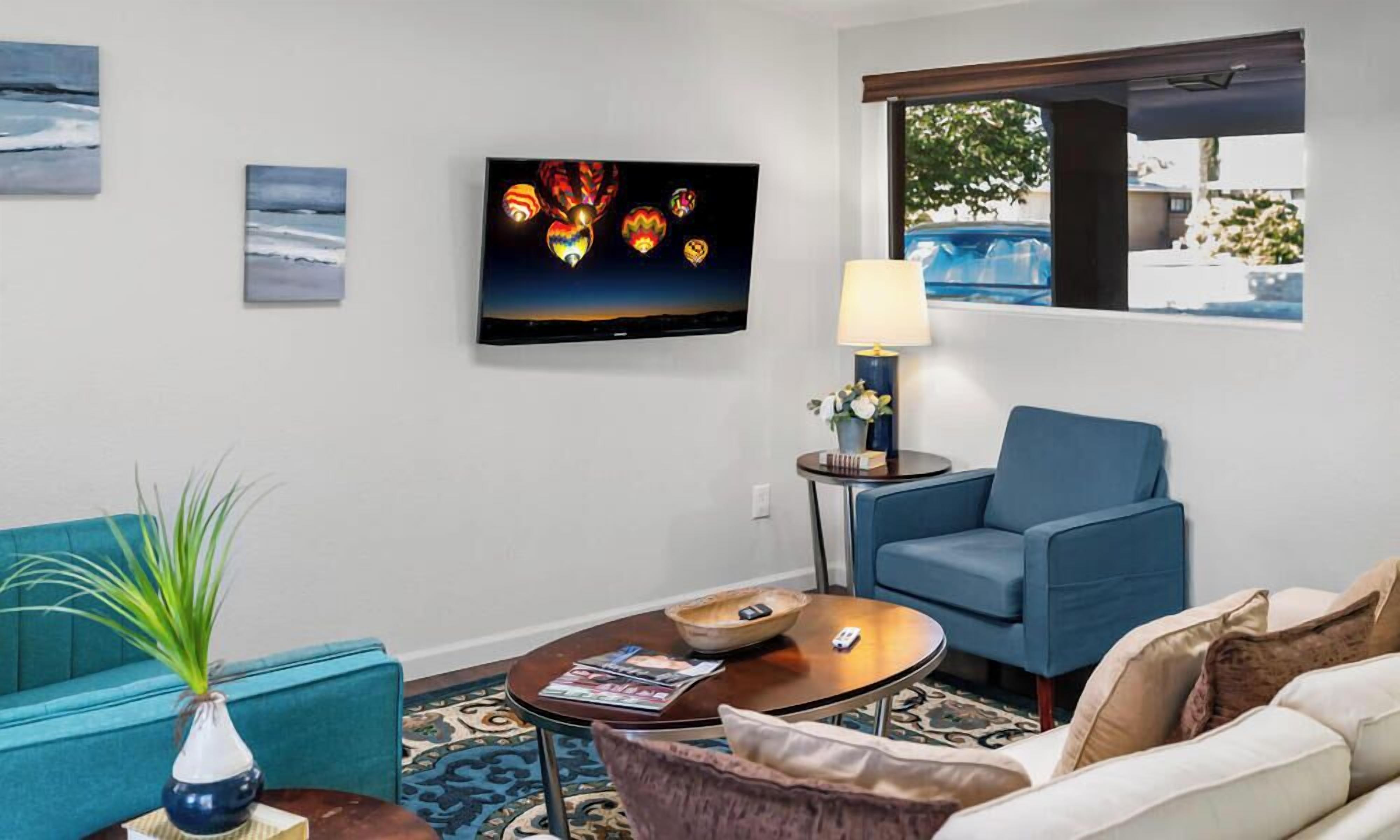 Ein Wohnzimmer mit Flachbildfernseher, blauem Sessel, Sofa, Couchtisch und einer Lampe.