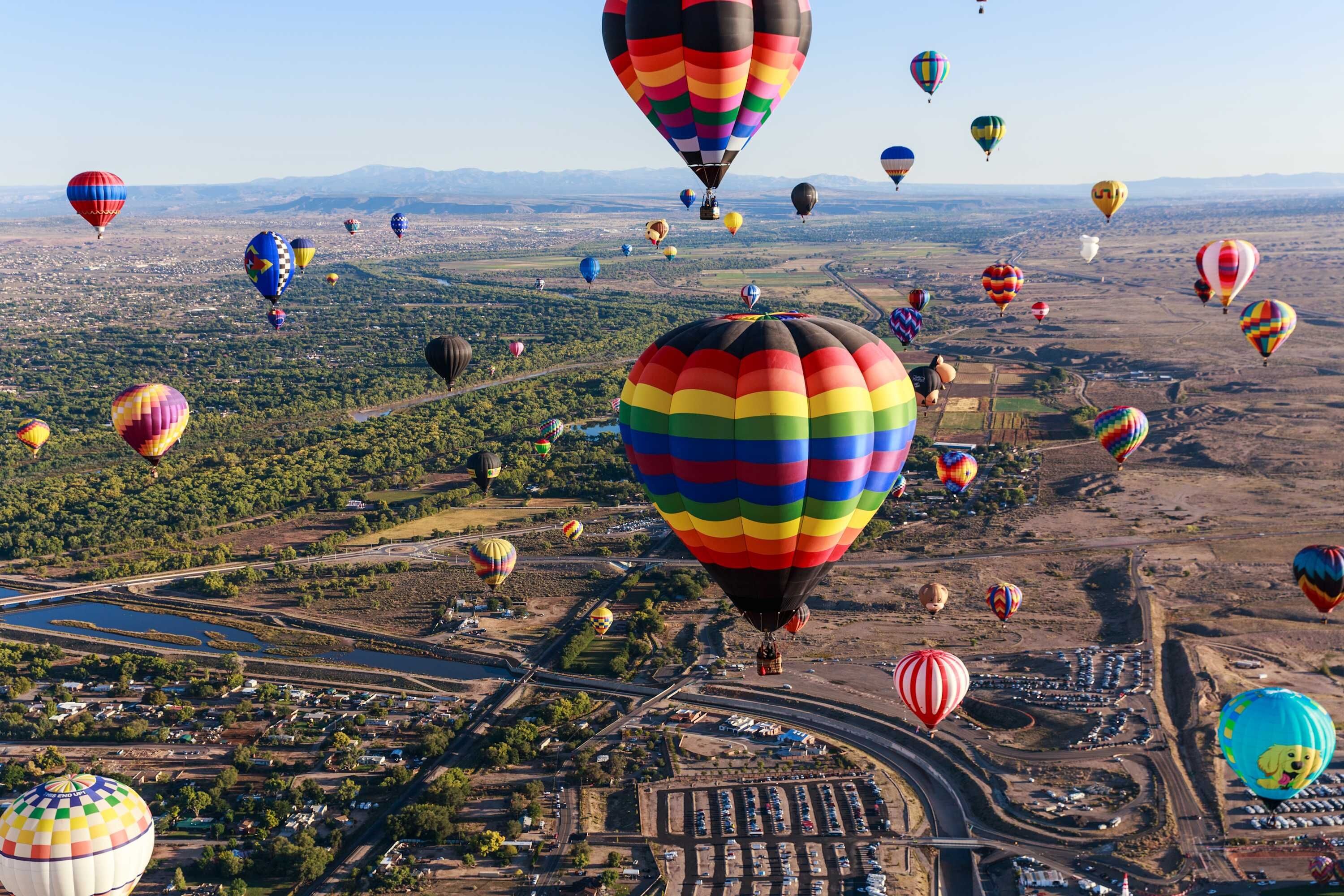A large number of hot air balloons over a cityscape with roads and buildings.
