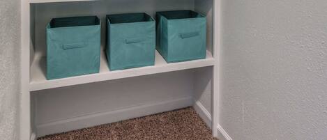 A closet with white walls and a carpeted floor, containing four teal storage bins on the shelves.