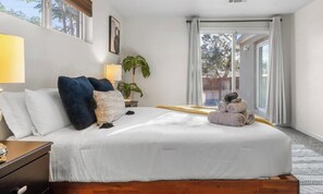 A bedroom with a bed, bedside lamps, a plant, and a view through a sliding door. - Pitt Paradise: Pet-Friendly Oasis - An Irvie Home (Albuquerque)