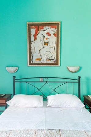 Un letto con lenzuola bianche, una parete color petrolio e un quadro astratto incorniciato sopra.