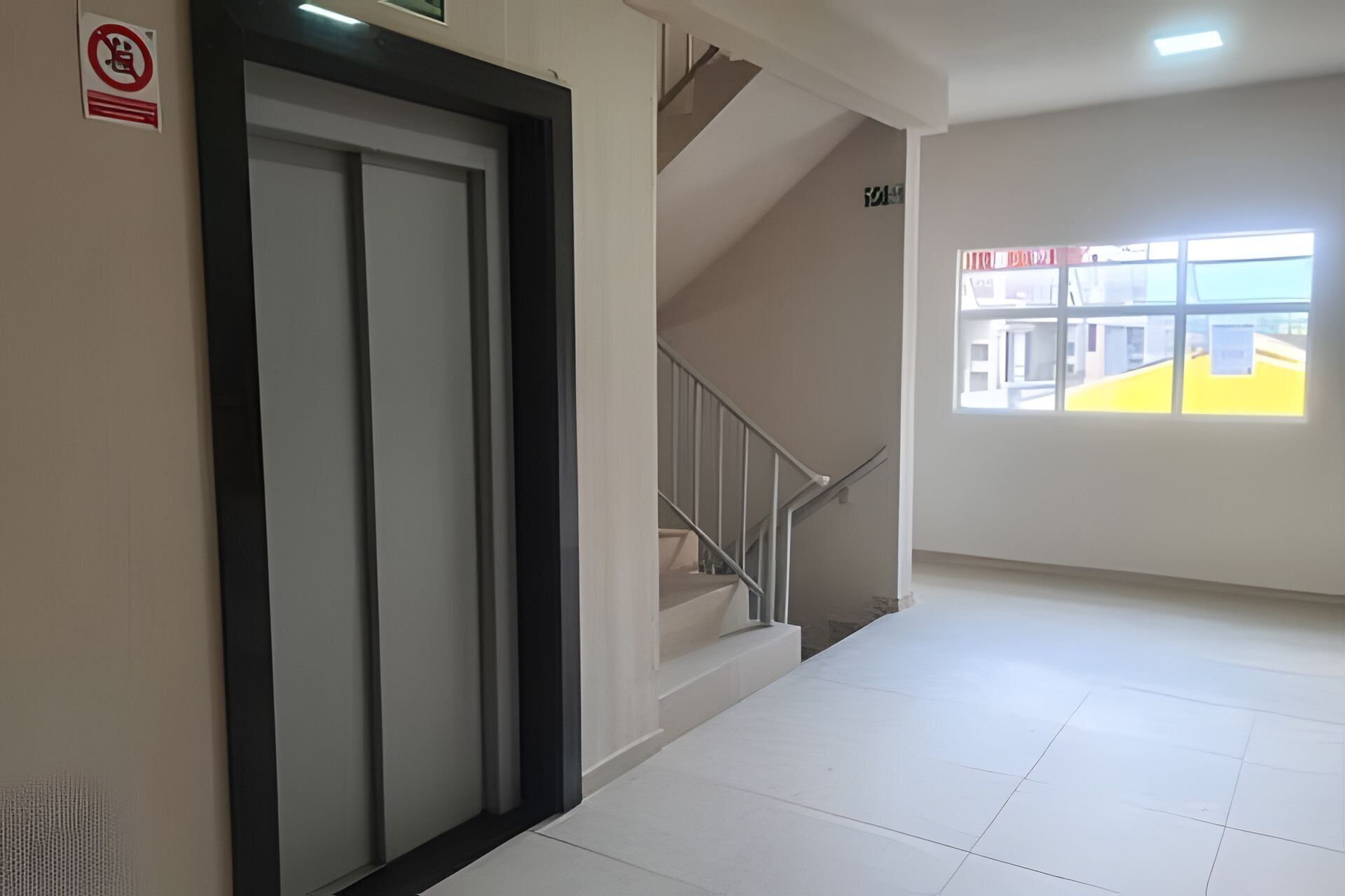 A hallway with a closed door, a staircase, and a window with a view of buildings.