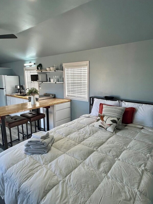 A compact bedroom with a bed, bedside table, and a small kitchenette area.