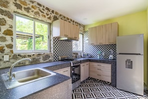 A kitchen with a stone wall, a sink, a stove, a refrigerator, and patterned tiles. - Escape to the countryside: Private House in Boutique Complex. (Tepoztlán)