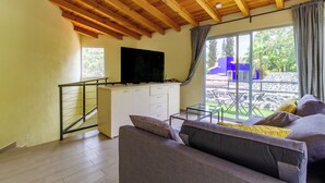 A living room with a wooden ceiling, a sofa, a TV on a white cabinet, and a view of the outdoors. - Escape to the countryside: Private House in Boutique Complex. (Tepoztlán)
