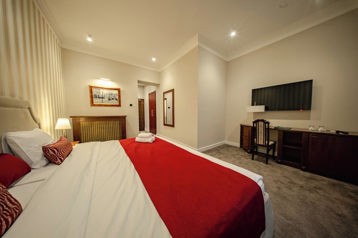 A hotel room with a large bed, a desk, a chair, a television, and a door leading to another room.