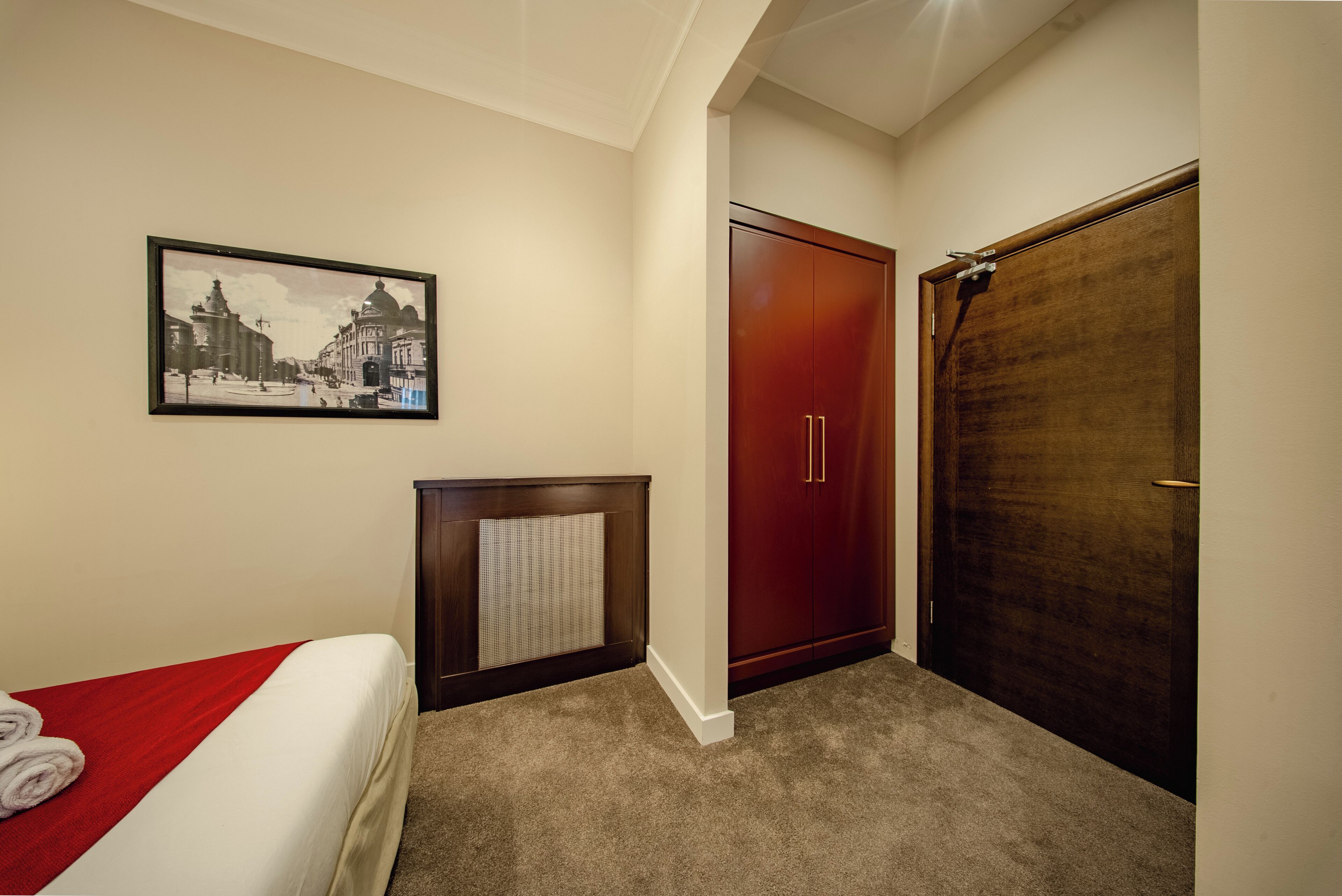 A hotel room with a bed, a radiator, a wardrobe, and a framed picture on the wall.
