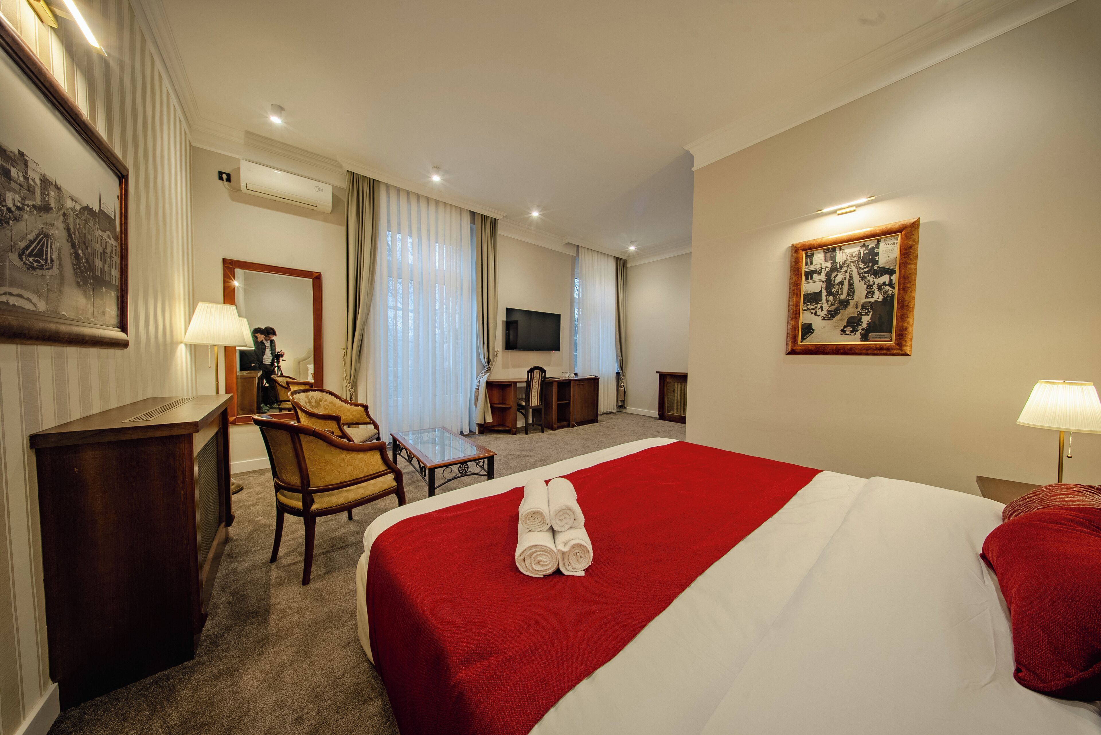 Een hotelkamer met een groot bed, een bureau, een stoel, een televisie en een ingelijst schilderij aan de muur.