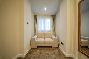 Une pièce étroite avec un canapé beige, un miroir et une fenêtre avec des rideaux.