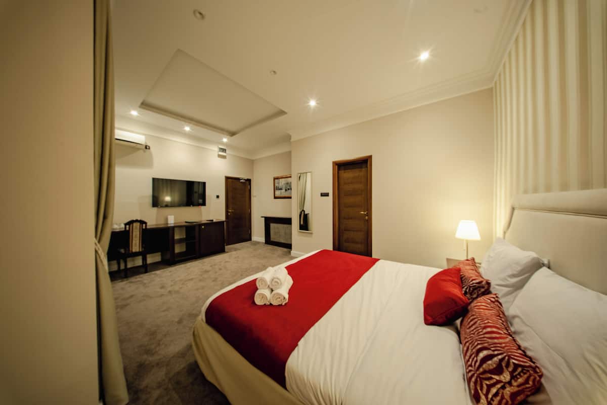 A hotel room with a neatly made bed, a desk with a chair, a television, and a fireplace.