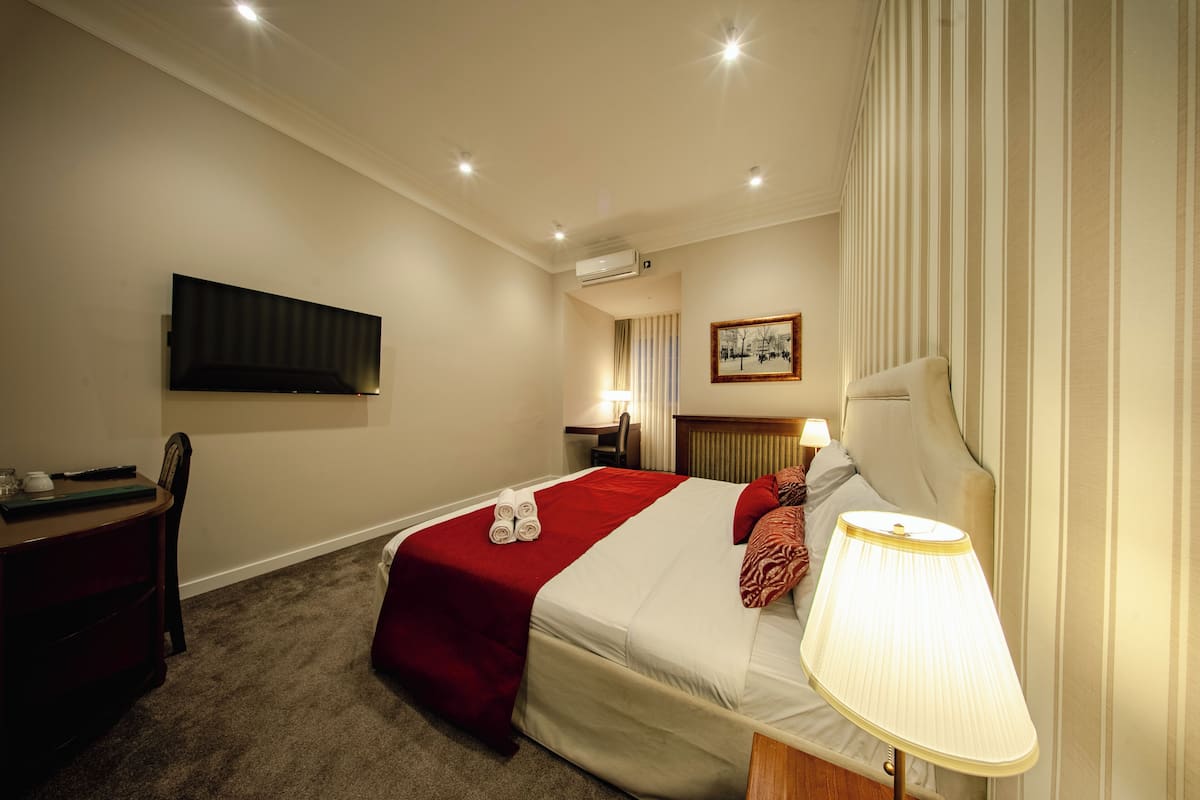 A hotel room with a bed, a desk, a chair, a TV, and a lamp.