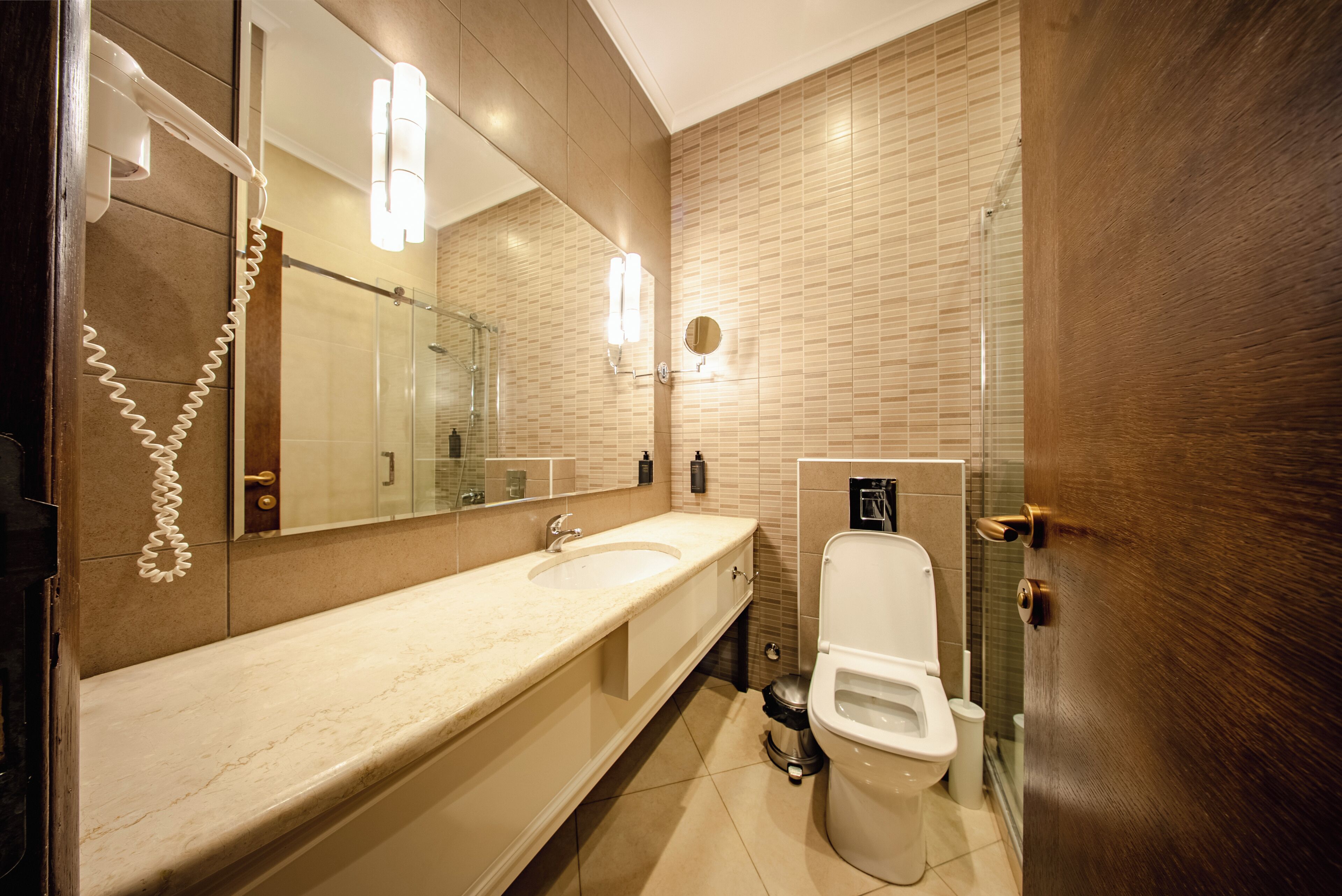 A modern bathroom with a large mirror, a sink, a toilet, and a shower area.
