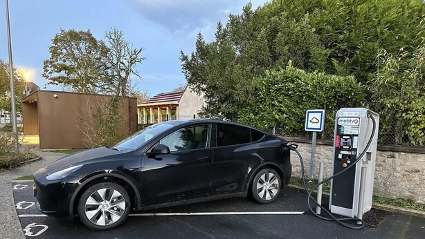 A black car parked at a charging station with a sign indicating it is a public charging point.