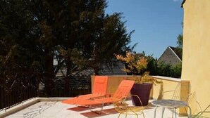 A patio with two orange lounge chairs, a purple planter, and a small table with a chair.