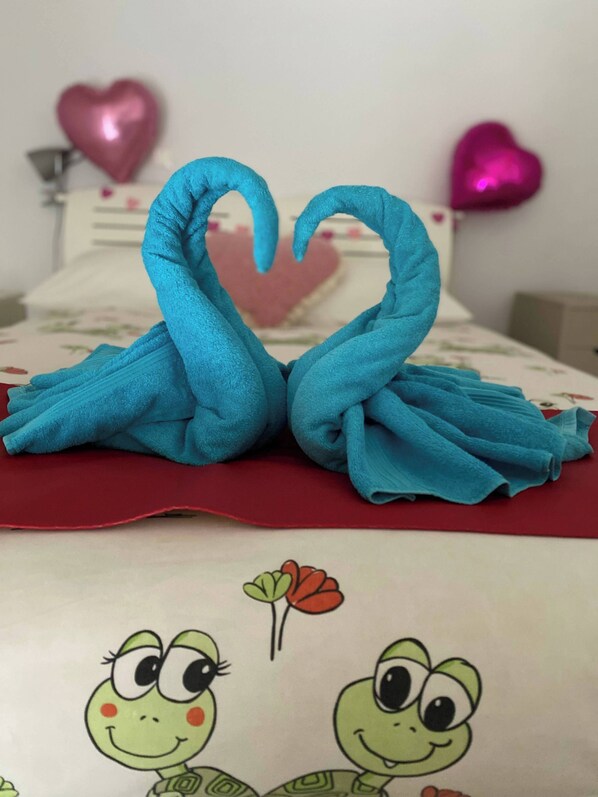 A bed with a red blanket, a heart-shaped towel arrangement, and cartoon turtle prints. - Tiny Loft with Garden View & Free Parking (Dun-le-Palestel)