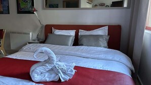 Una habitación de hotel con cama, almohadas, una manta roja, una toalla blanca, una lámpara de escritorio y un espejo.