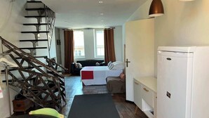 Et kompakt hotelværelse med seng, lille siddeområde, tekøkken og trappe.