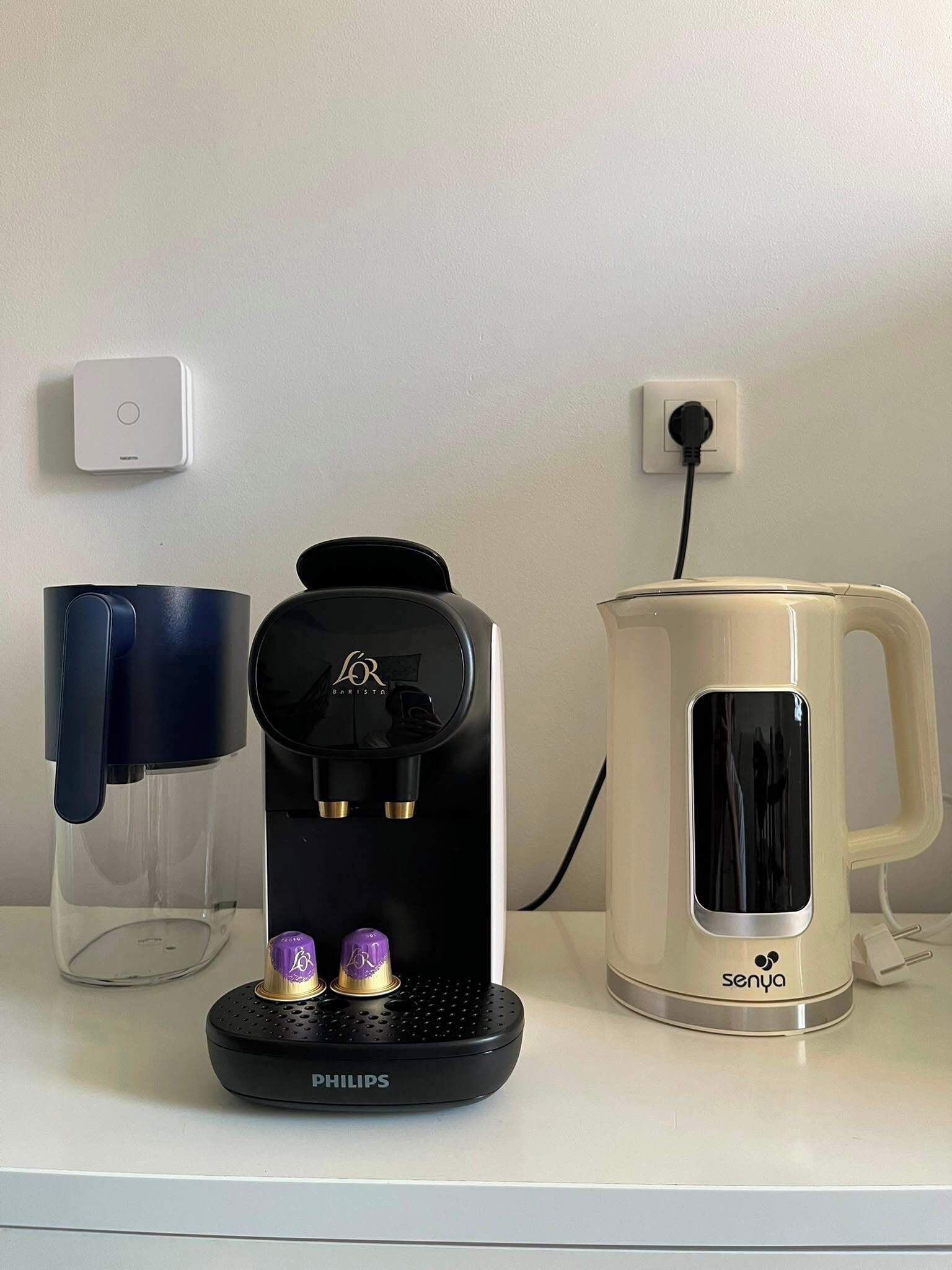 Een koffiezetapparaat, een mok en een stopcontact op een witte ondergrond.