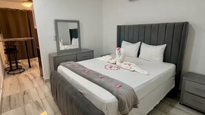 Een netjes ingerichte hotelkamer met een groot bed, een nachtkastje, een spiegel en een zithoek met een stoel en tafeltje.