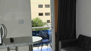 Een ruimtelijk ingerichte woonruimte met kitchenette, een eethoek en een balkon met uitzicht op gebouwen en groen.
