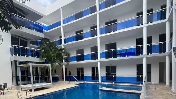 Een hotel met meerdere verdiepingen, een centraal gelegen zwembad, balkons met blauwe leuningen en palmbomen.