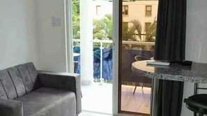 Sala moderna com sofá cinza, cozinha com bancada de granito e varanda com mesa e cadeiras.