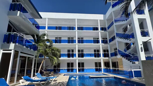 Ein mehrstöckiges Hotel mit Schwimmbad, Balkonen mit blauen Rahmen und Palmen.