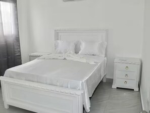 Quarto branco com cama, mesas de cabeceira e cómoda.