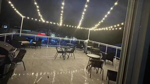 En udendørs terrasse med lyskæder, borde og stole.