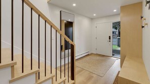 Ein modernes Interieur mit einer Holztreppe, einer zur Außenseite führenden Tür und einem sichtbaren Außenbereich.