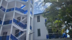 Un edificio de varios pisos con paredes exteriores blancas y detalles azules, que cuenta con una escalera central y balcones.