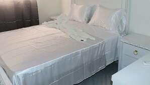 Una cama bien tendida con sábanas blancas y una toalla doblada en forma de cisne.