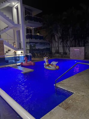 A swimming pool with a blue tint, surrounded by a modern building with a staircase and a mural of a beach scene. - Apartment Near the Pool in the Heart of Sosua 106 (Sosúa)
