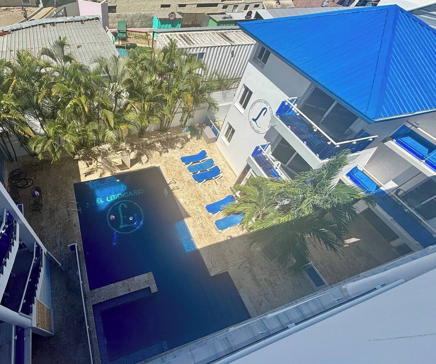 A pool area with lounge chairs, palm trees, and a building with a blue roof.