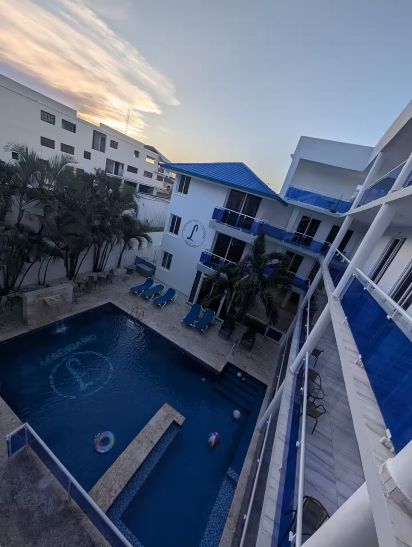 Un área de piscina con sillones de descanso, fuente de agua y un edificio con balcones.