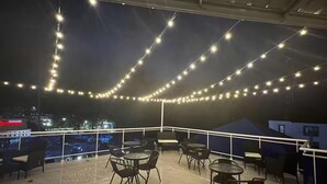 Une terrasse extérieure agrémentée de guirlandes lumineuses, de tables et de chaises.