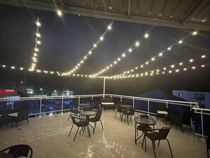 Une terrasse extérieure agrémentée de guirlandes lumineuses, de tables et de chaises.