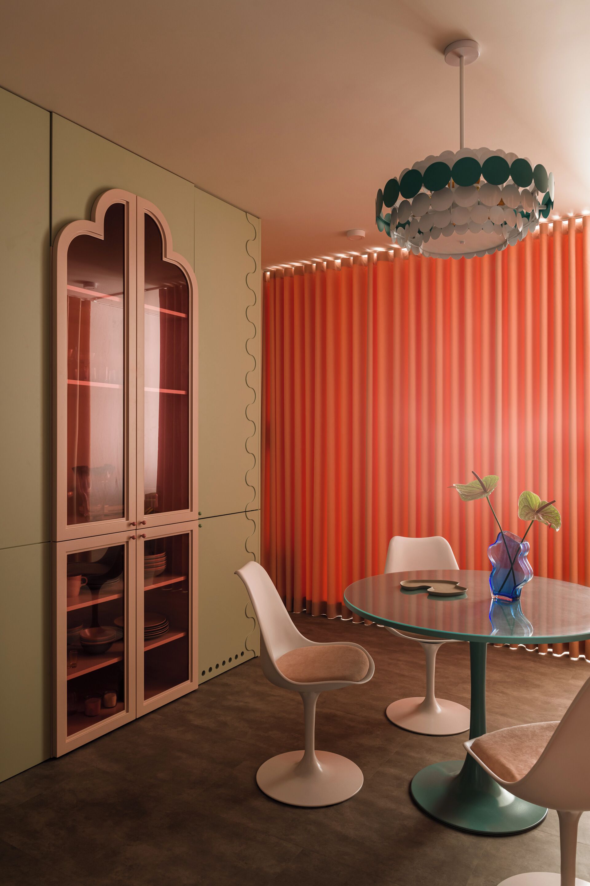 Un'area pranzo con tavolo in vetro, sedie bianche, un armadio con ante in vetro e un lampadario di design.