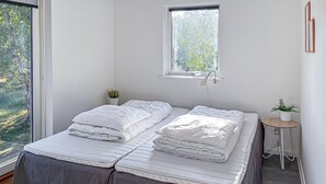 Ein Zimmer mit einem Bett, einem kleinen Tisch, einer Topfpflanze und einem Fenster mit Blick ins Grüne.