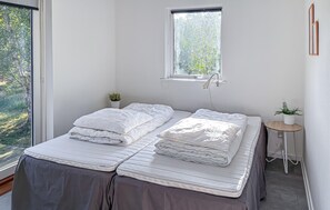 A room with a bed, a small table, a potted plant, and a window with a view of greenery.