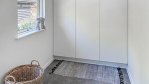 Ein Zimmer mit Fenster, einem Korbwäscheschrank, einem grauen Teppich und weißen Schränken.
